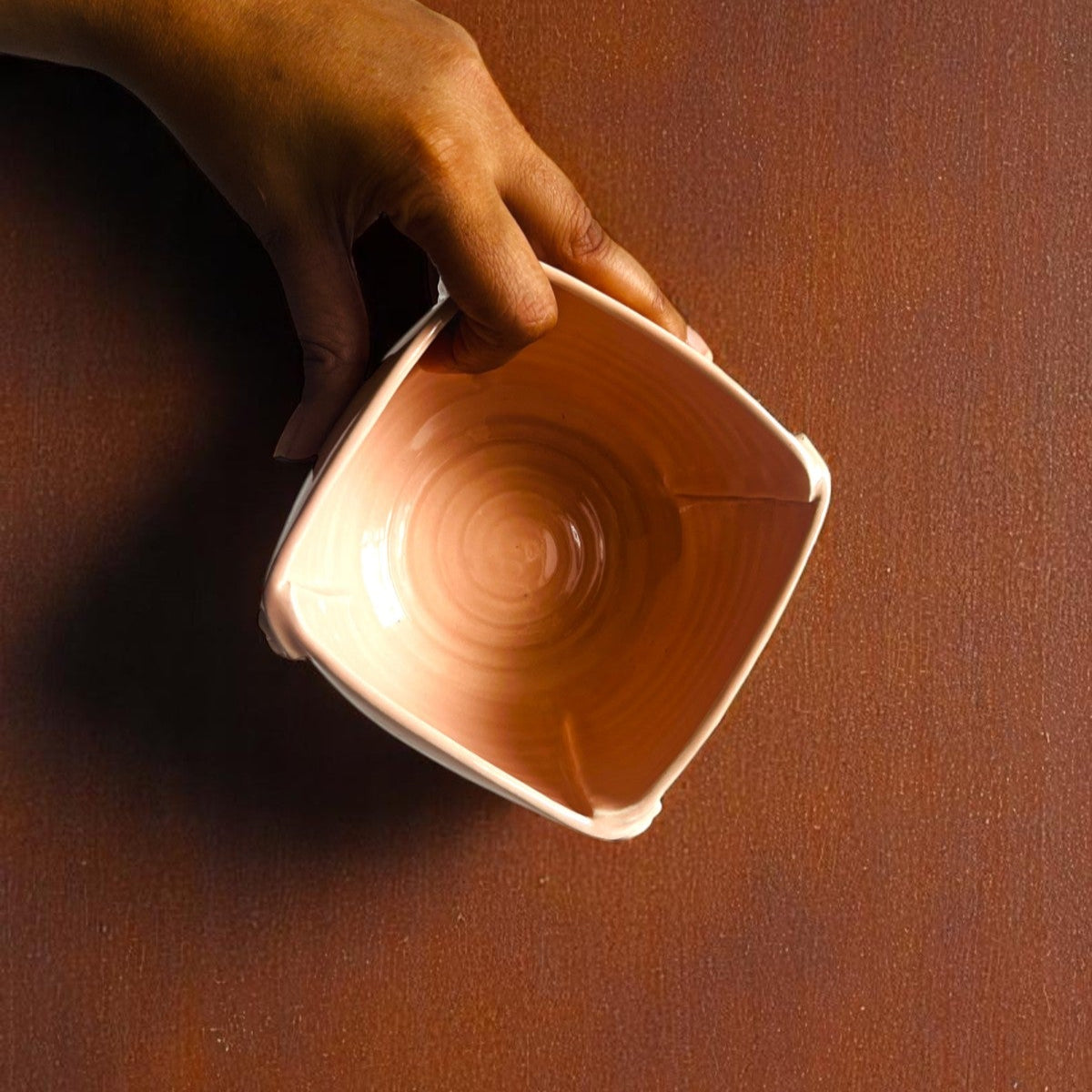 Hand holding a pink ceramic bowl on a wooden surface