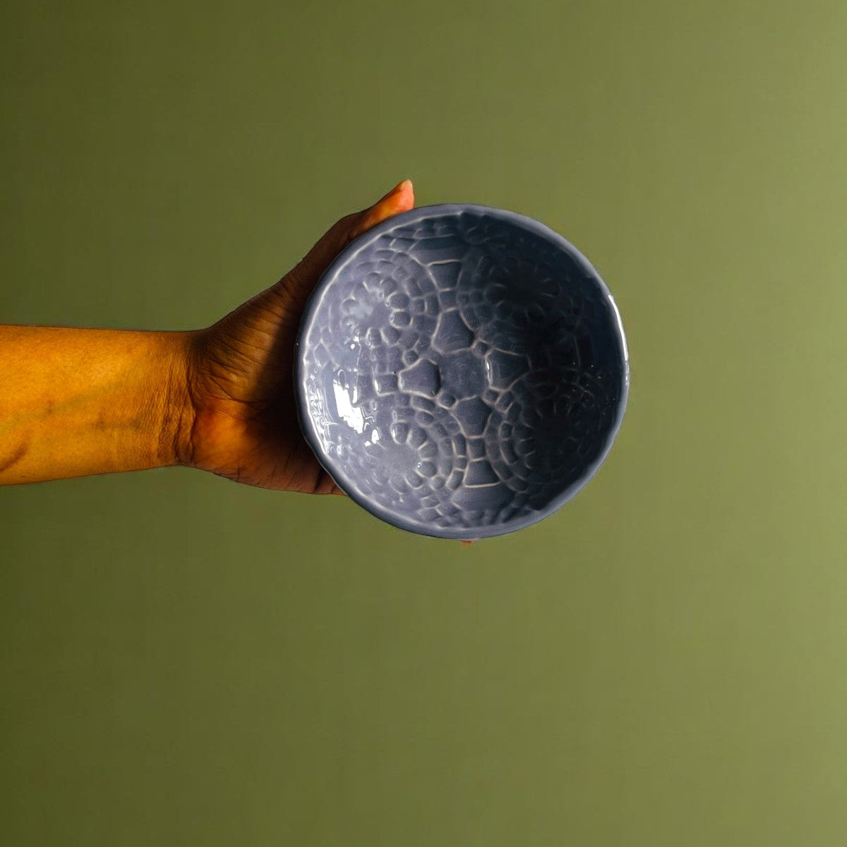 Hand holding a textured blue ceramic bowl against a green background