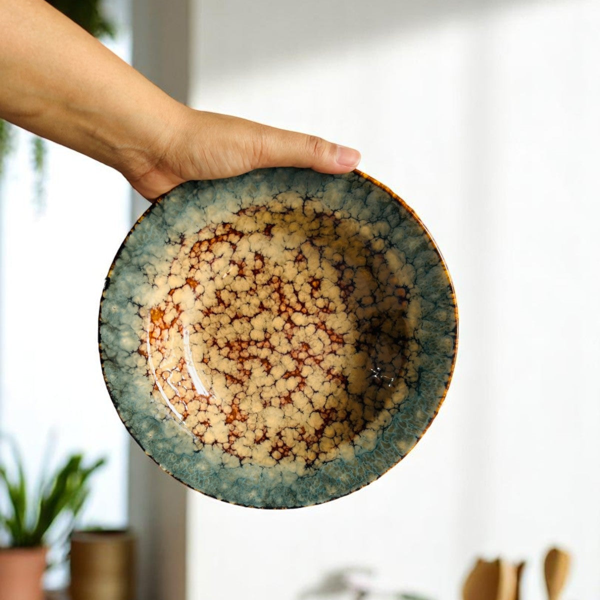 Hand holding a ceramic plate with a unique glaze pattern against a blurred indoor background