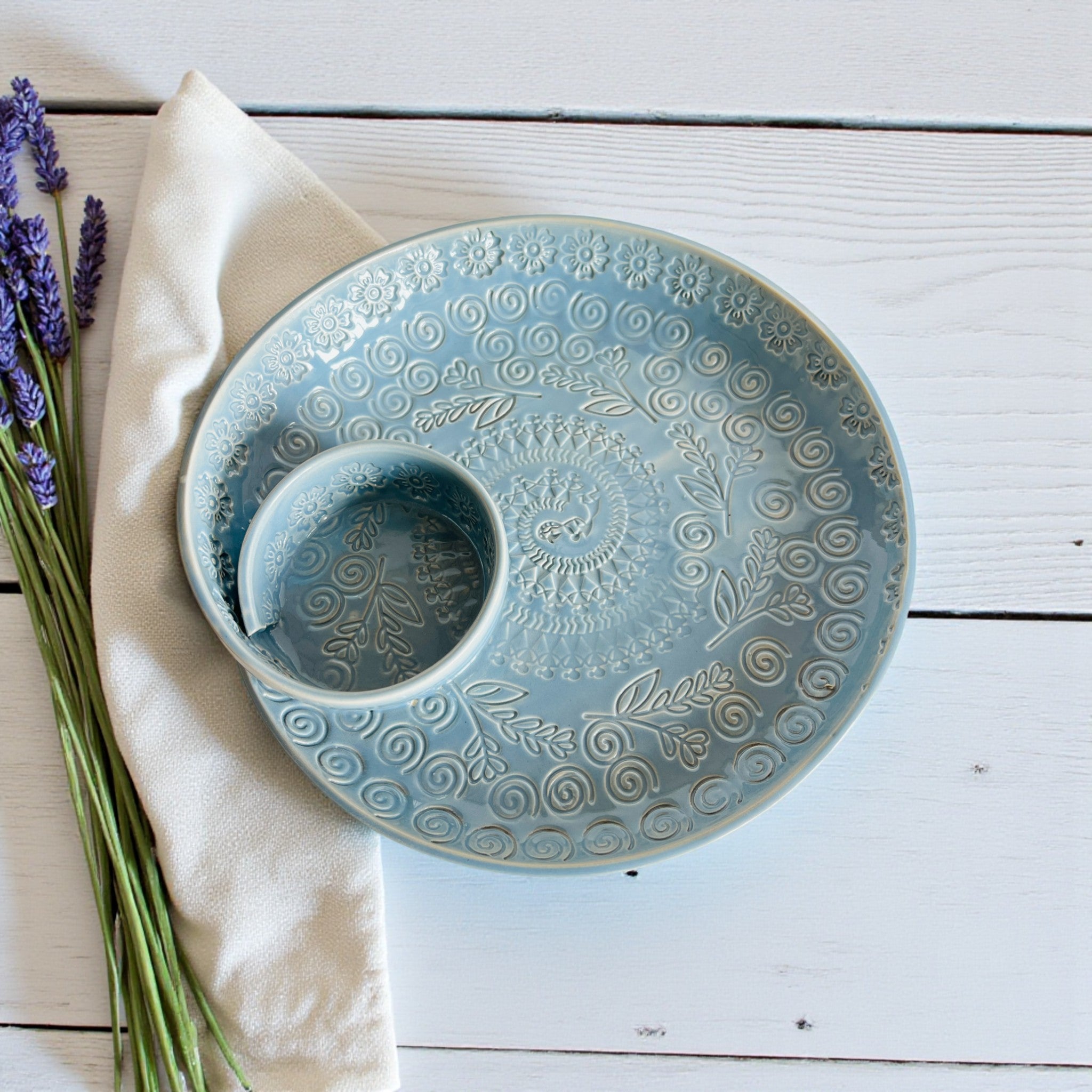 Decorative ceramic plate with embossed patterns on a wooden surface with lavender flowers.