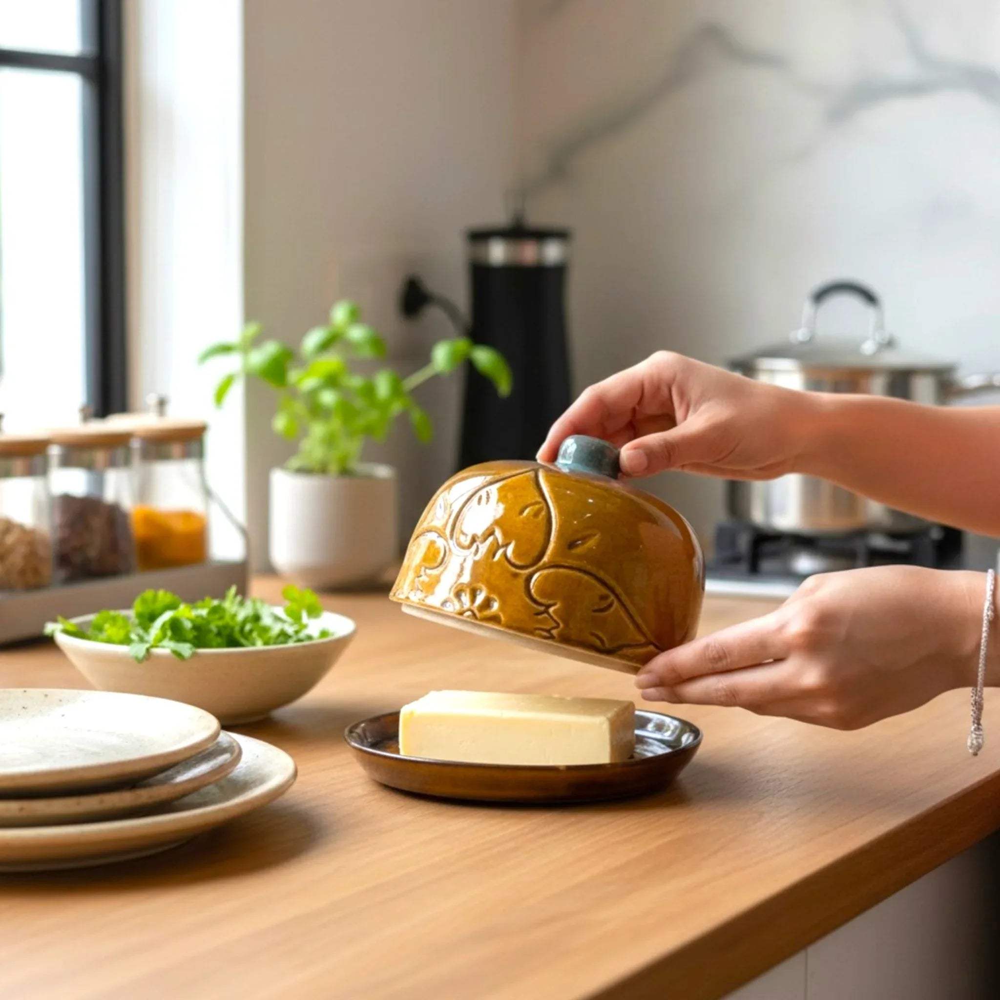 Breakfast scene; Vintage Amber Butter Dish next to a bowl of fresh herbs and ceramic plates on a sunlit counter.