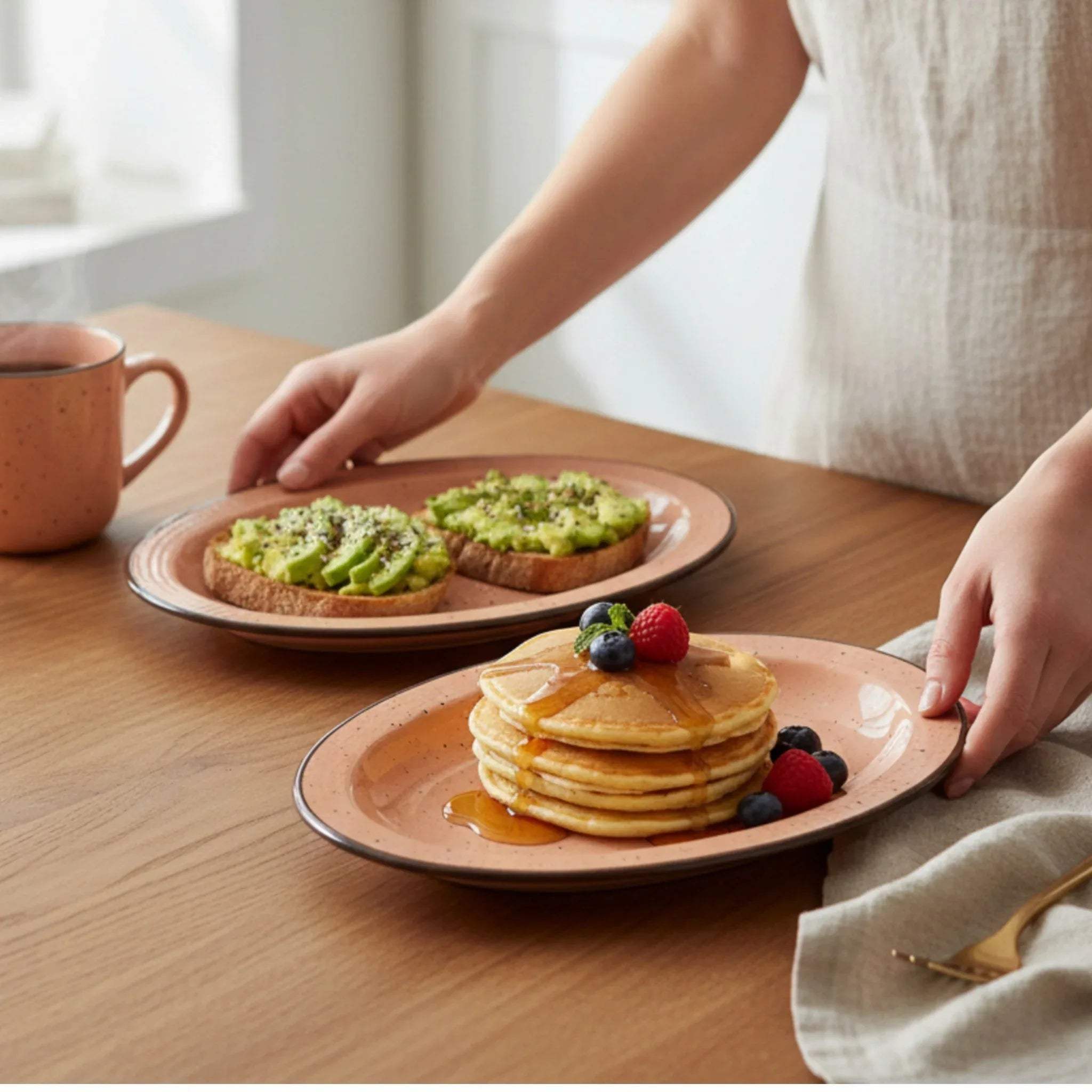 Person serving pancakes and avocado toast on the pink / peach ceramic plates on a wooden table.