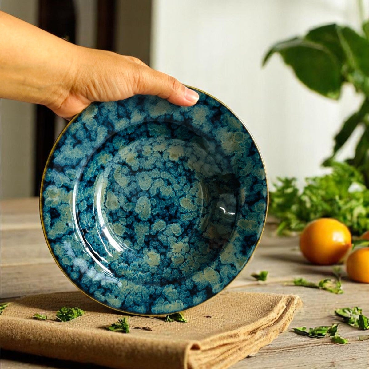 Hand holding a artisanal stoneware plate / bowl to demonstrate the size and show the blue-green product glazing.
