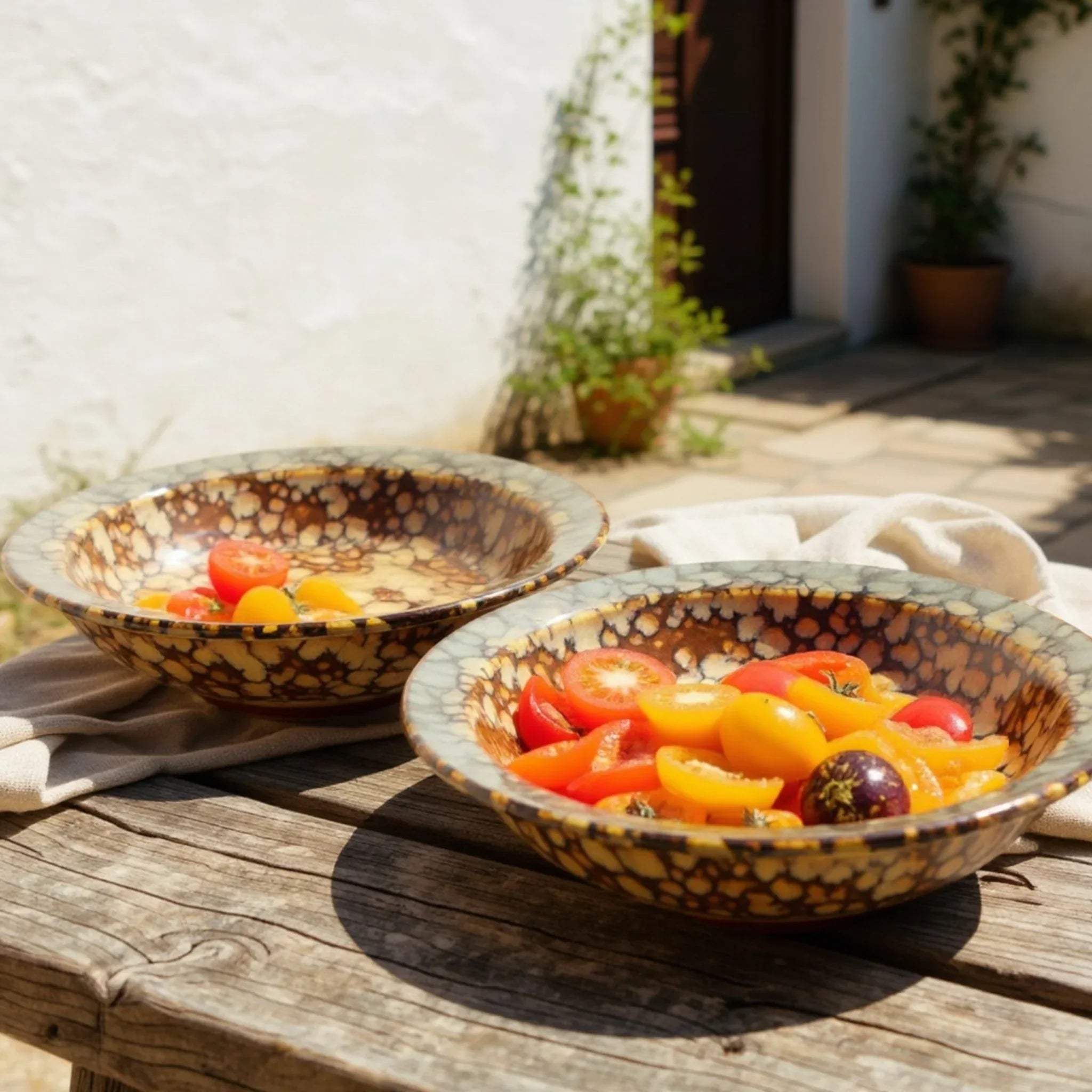 Two ceramic brown bowls cum plates  filled with colorful tomatoes on a wooden table outdoors.