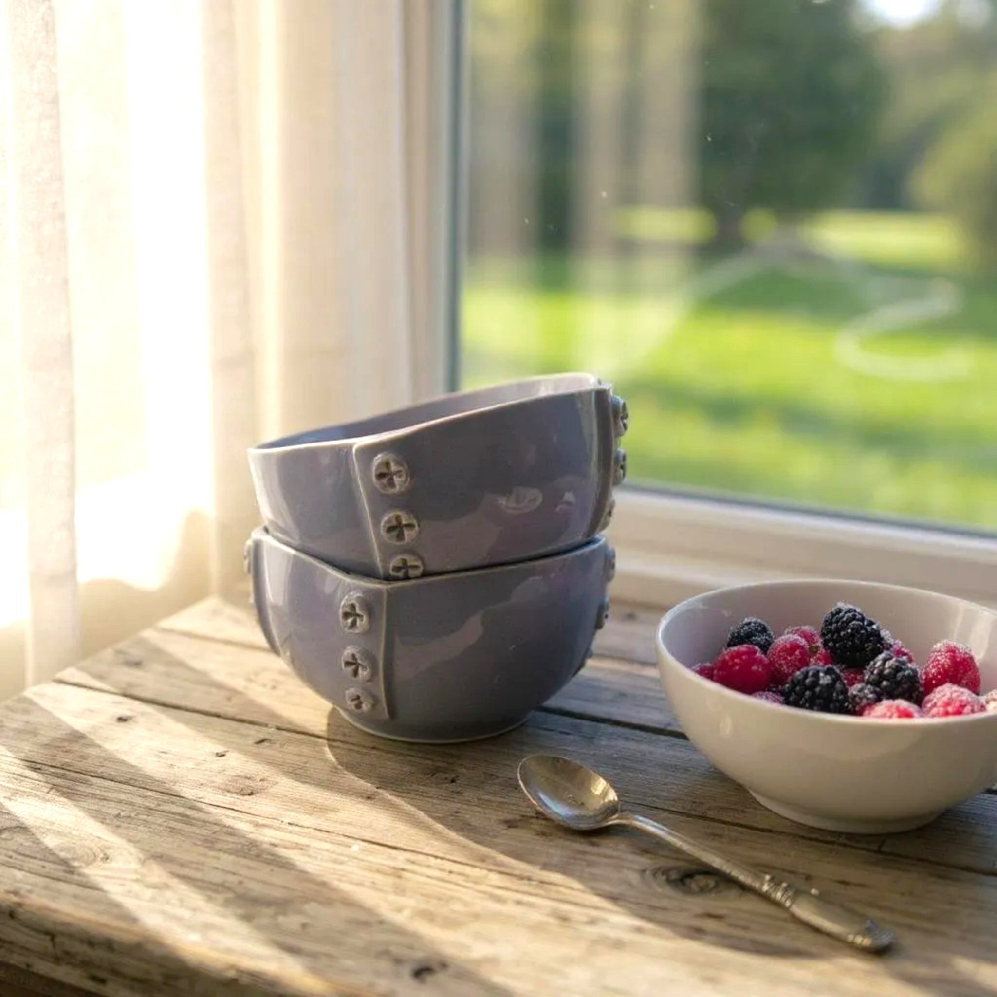 Two purple bowls with decorative studs on a wooden surface next to a bowl of berries.