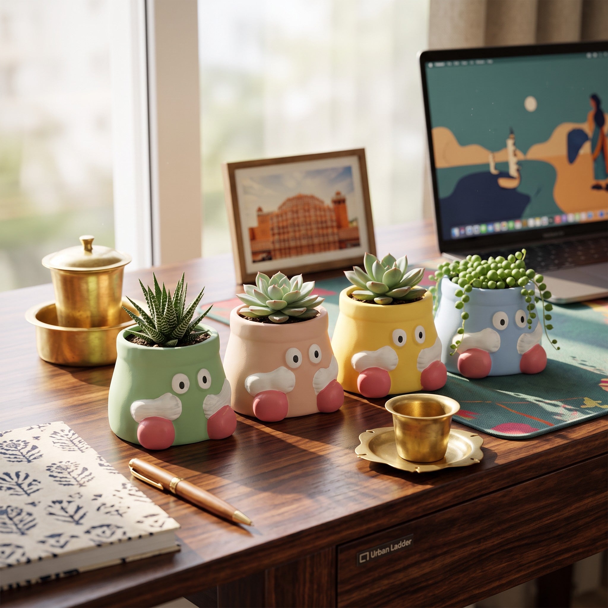 Four cute cartoon-style ceramic planters with animal faces in pastel green, pink, yellow, and blue, arranged on a wooden desk with a laptop, notebook, and small brass cup in a bright home office setting.