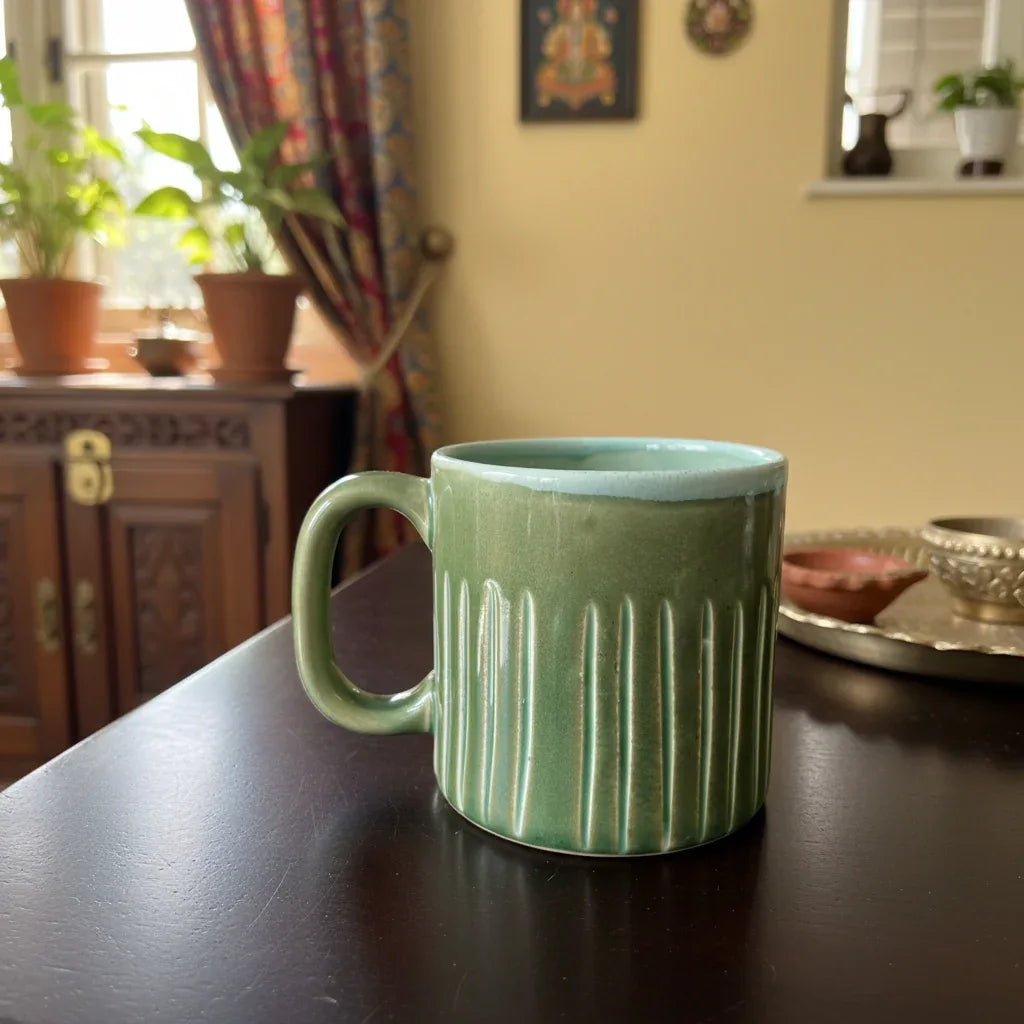 Green ceramic mug on a wooden table with a homey background.