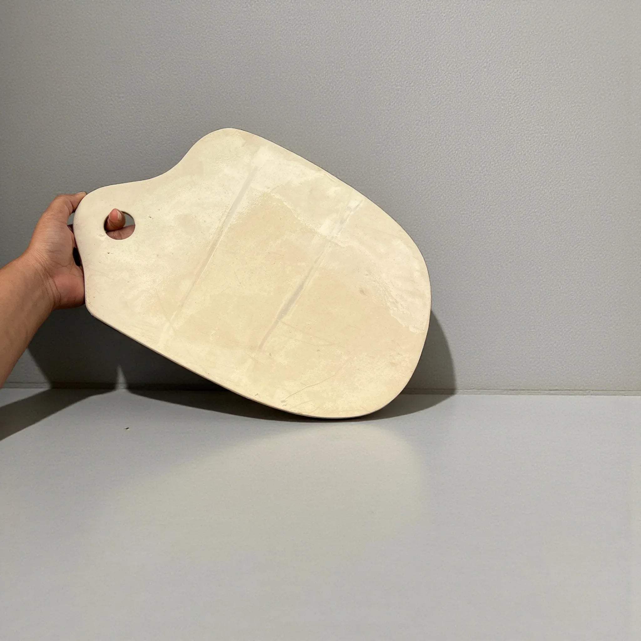 Back view; Hand holding a wooden cutting board against a gray background.