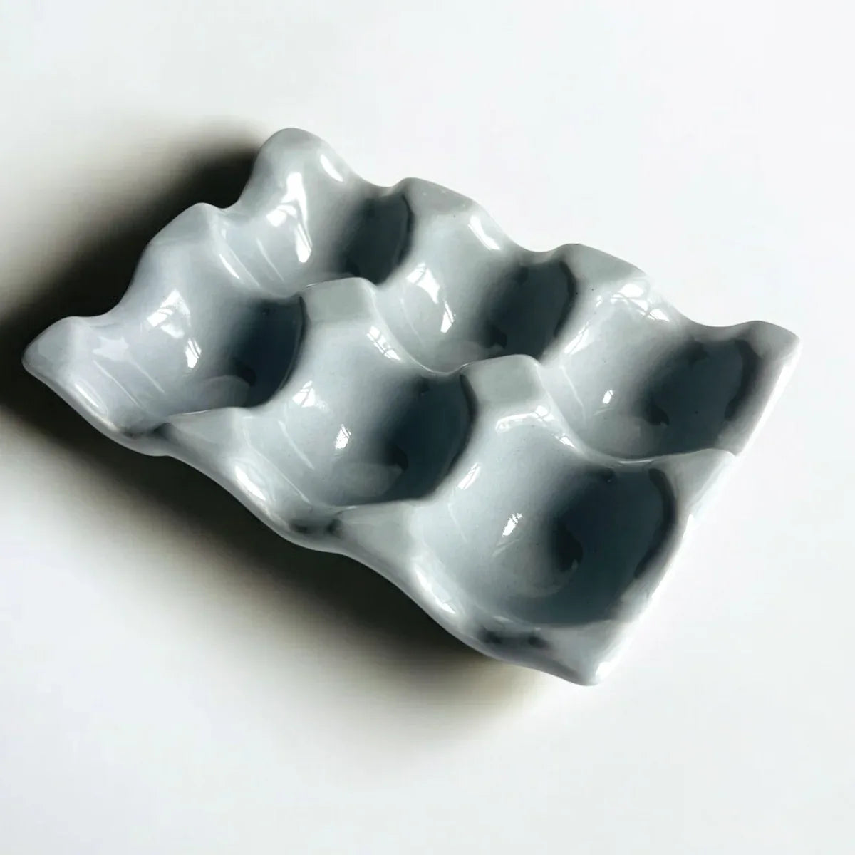 Smooth grey-blue ceramic glaze; scalloped 6-egg holder details and artisanal pottery finish for mood boards.
