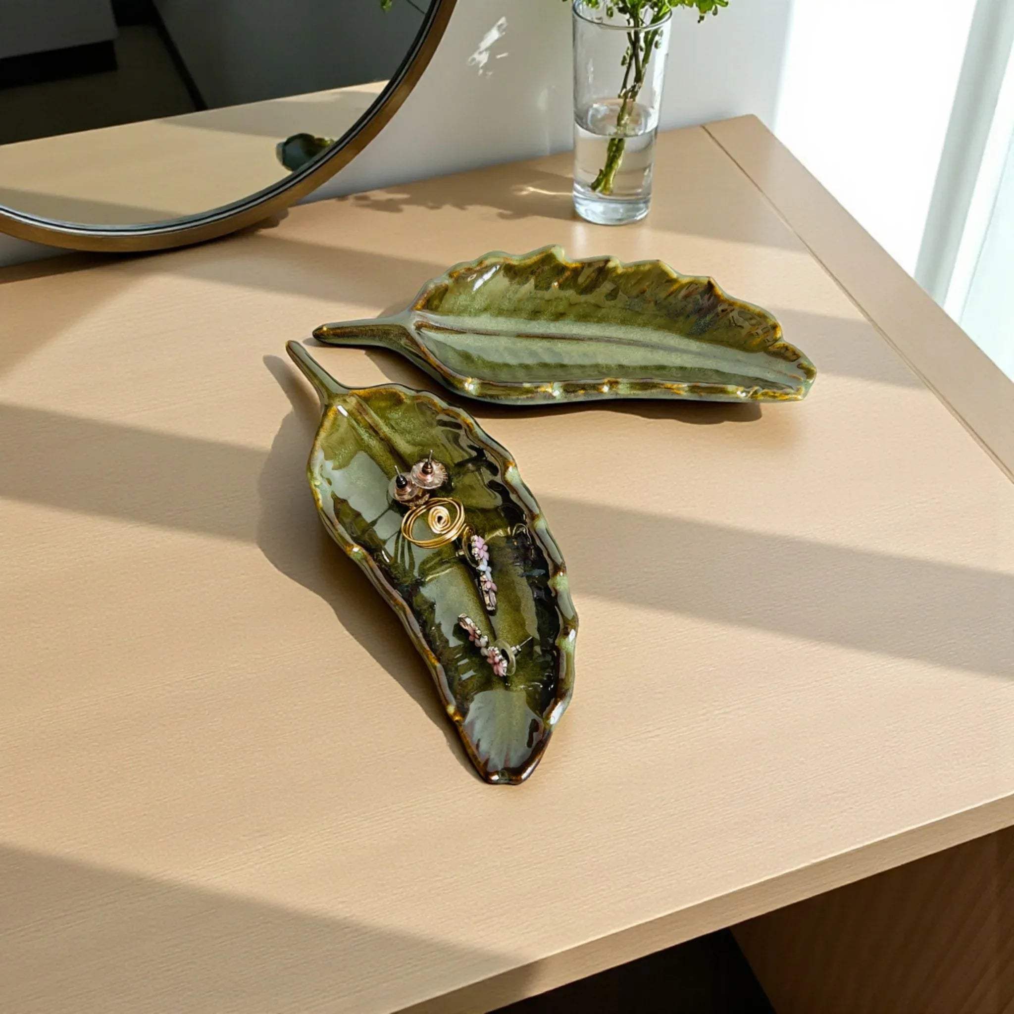 Entryway catch-all; a leaf tray placed on a console table holding jewellery and loose change near a mirror.