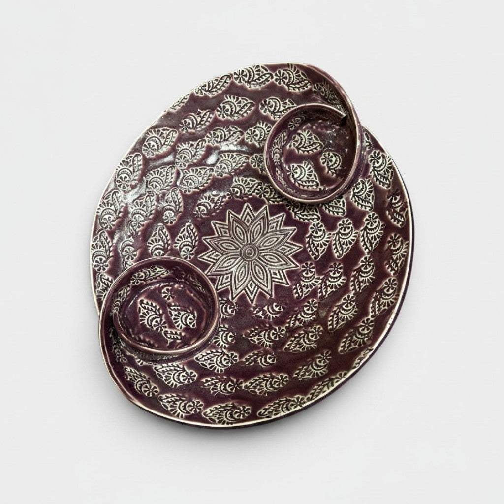 A detailed close-up of the crisp white hand-graved floral mandala motif cut into the deep purple glazed ceramic tray.