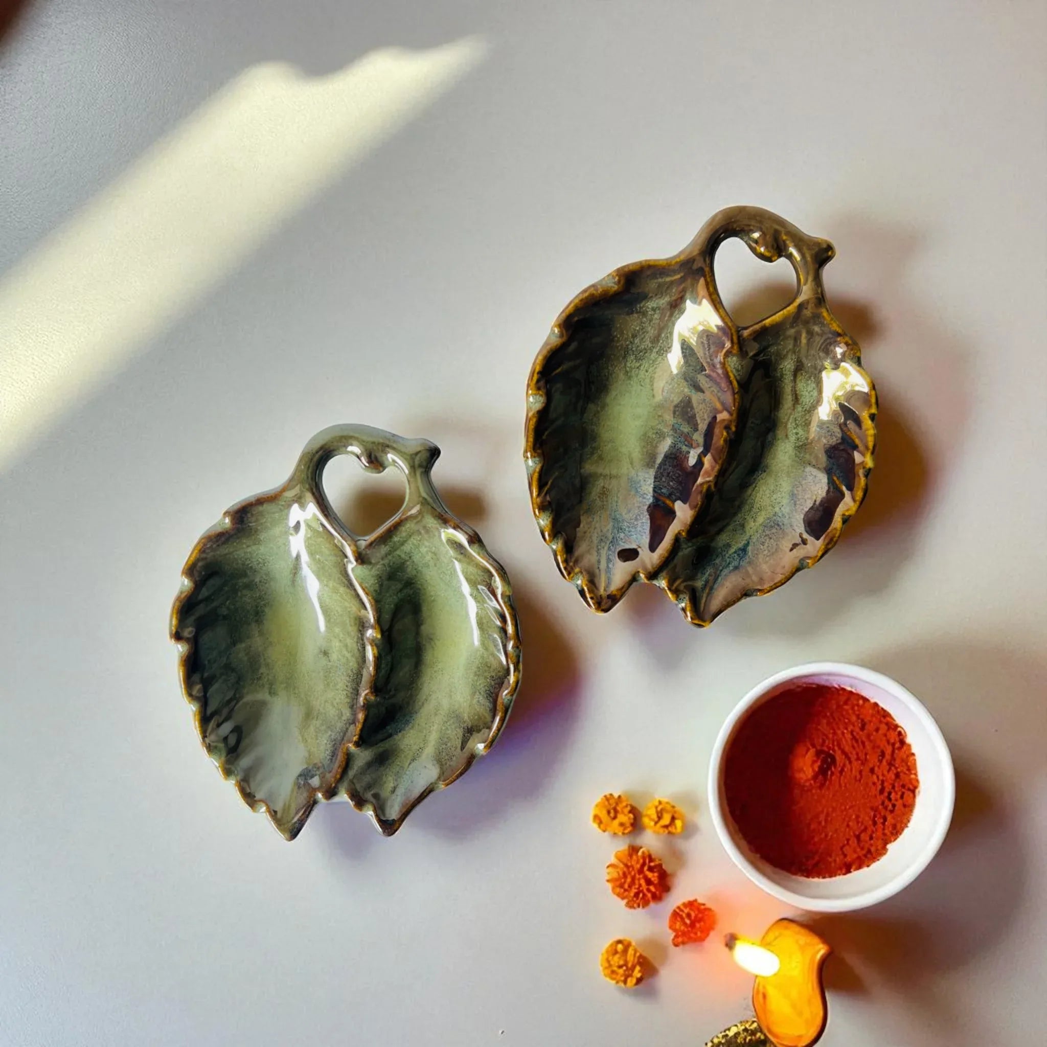 Roli Chawal Divided Tray; two leaf-shaped ceramic ritual dishes in earthy green and blue glazes.