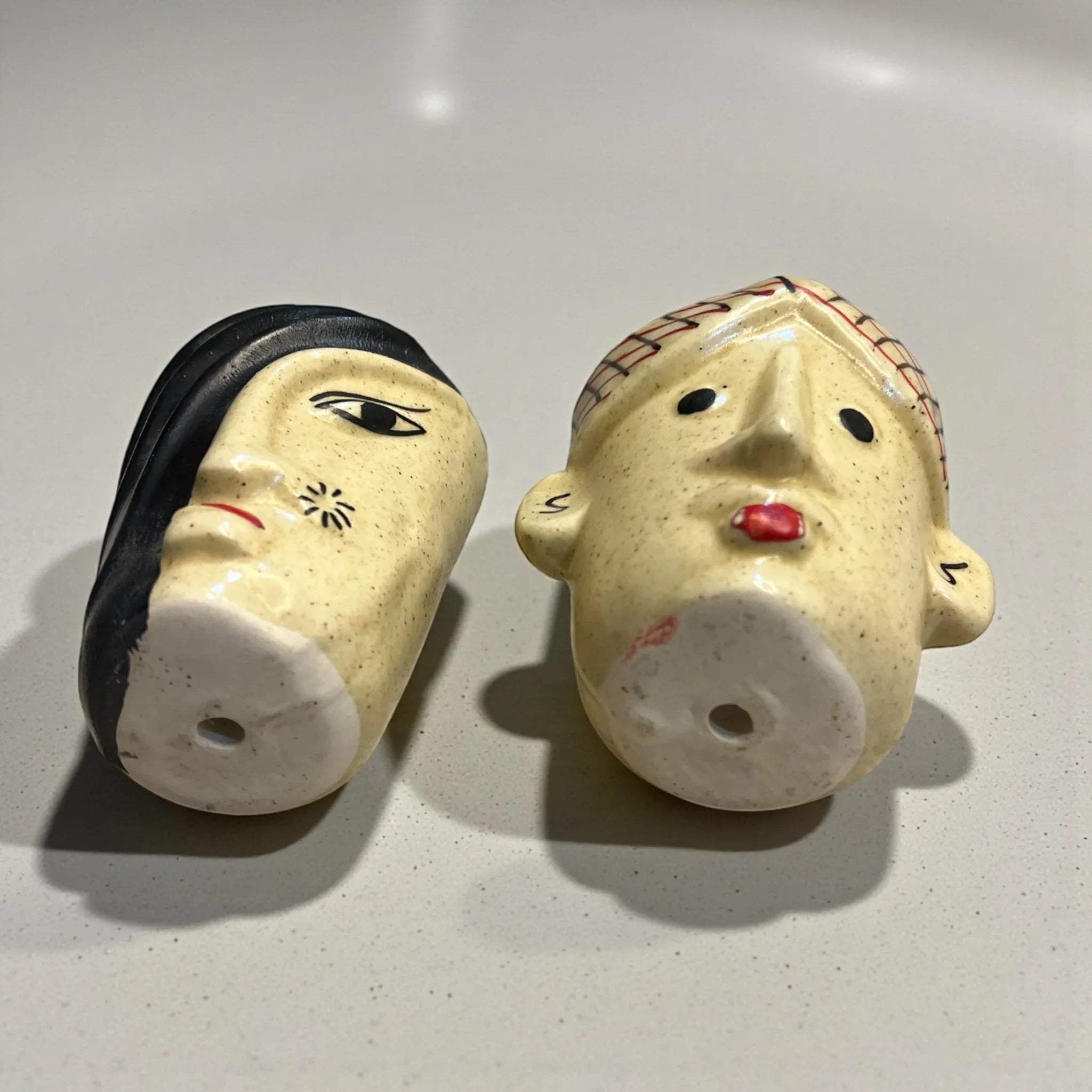 Two ceramic face figurines on a light gray background with drainage holes for healthy succulents.