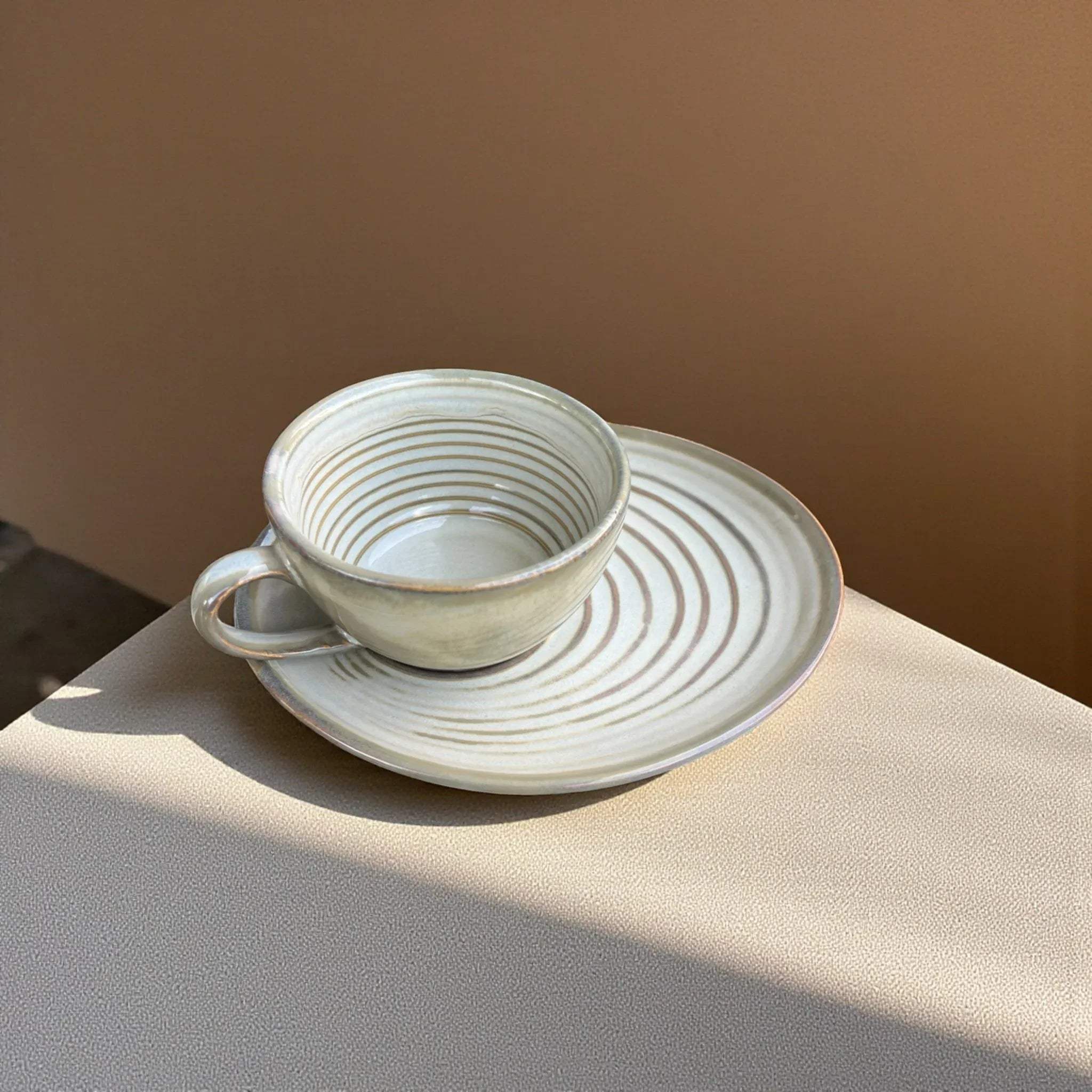 Brown ceramic cup and saucer set on a neutral surface with a warm brown background.