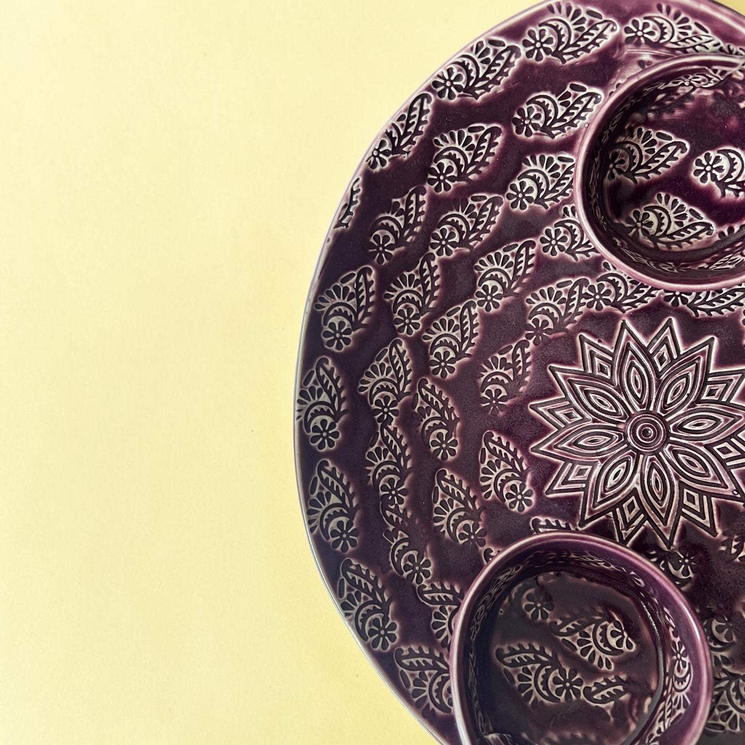 An organic oval plum purple ceramic serving platter featuring hand-graved paisley patterns and a central flower mandala.