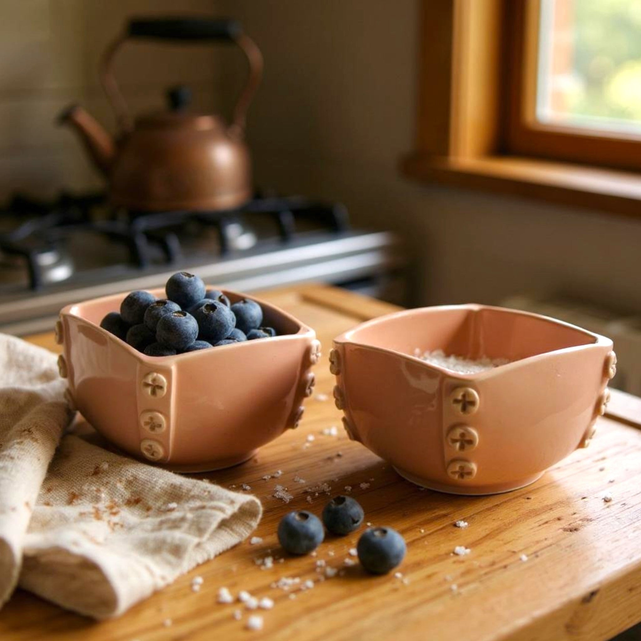 Two pink ceramic bowls on a wooden surface with blueberries and salt, aesthetic kitchen setting.