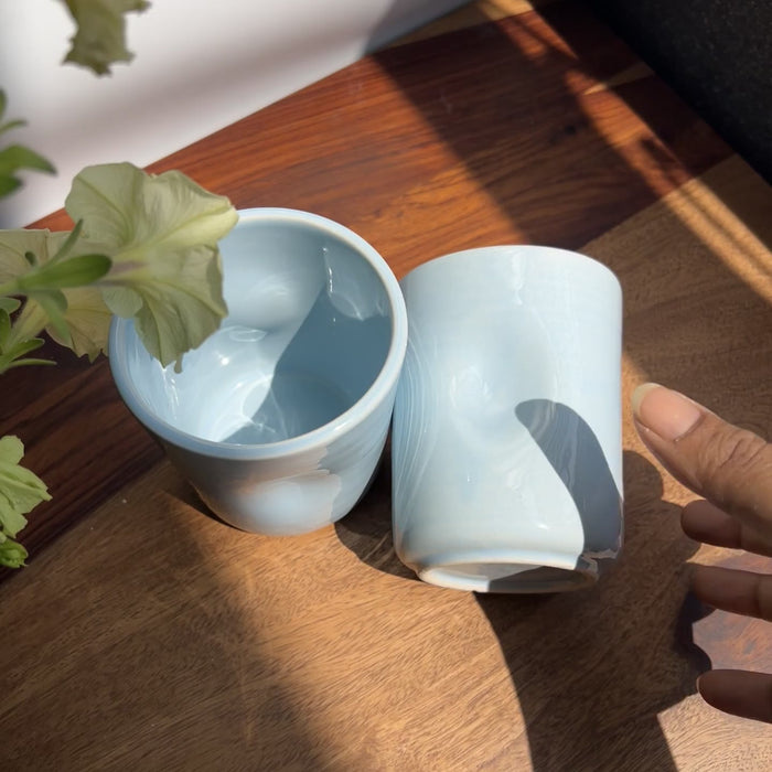 Sky blue glaze of the ceramic glasses in focus showing the raw video and the natural thumb print for easy holding.
