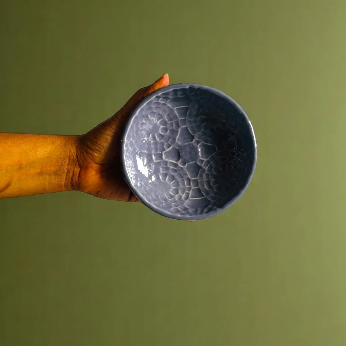 Hand holding a textured purple ceramic bowl against a green background for size reference.