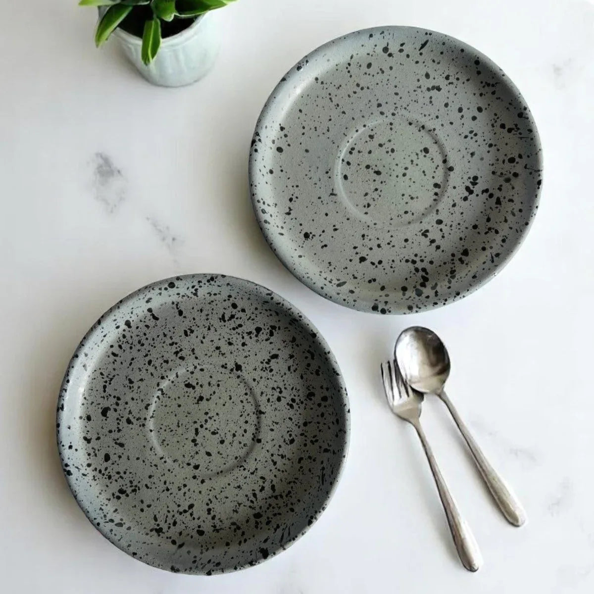 Rustic Stone artisanal speckled stoneware plates with fork and spoon on a white table.