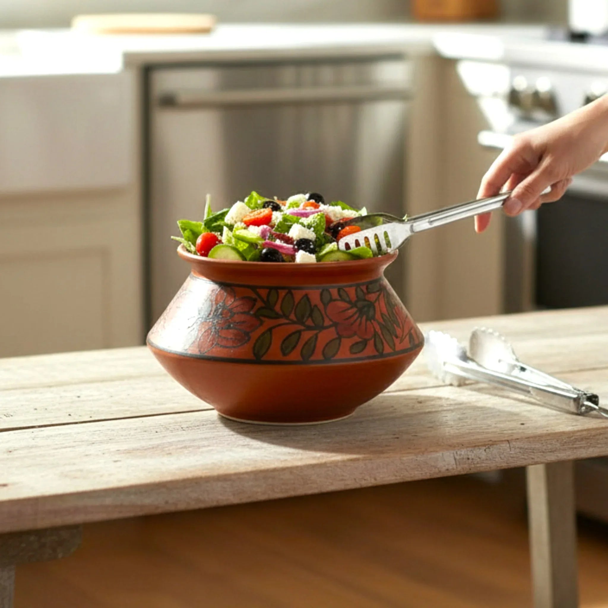 Artisan ceramic bowl with floral design holding fresh salad on rustic wood table in kitchen