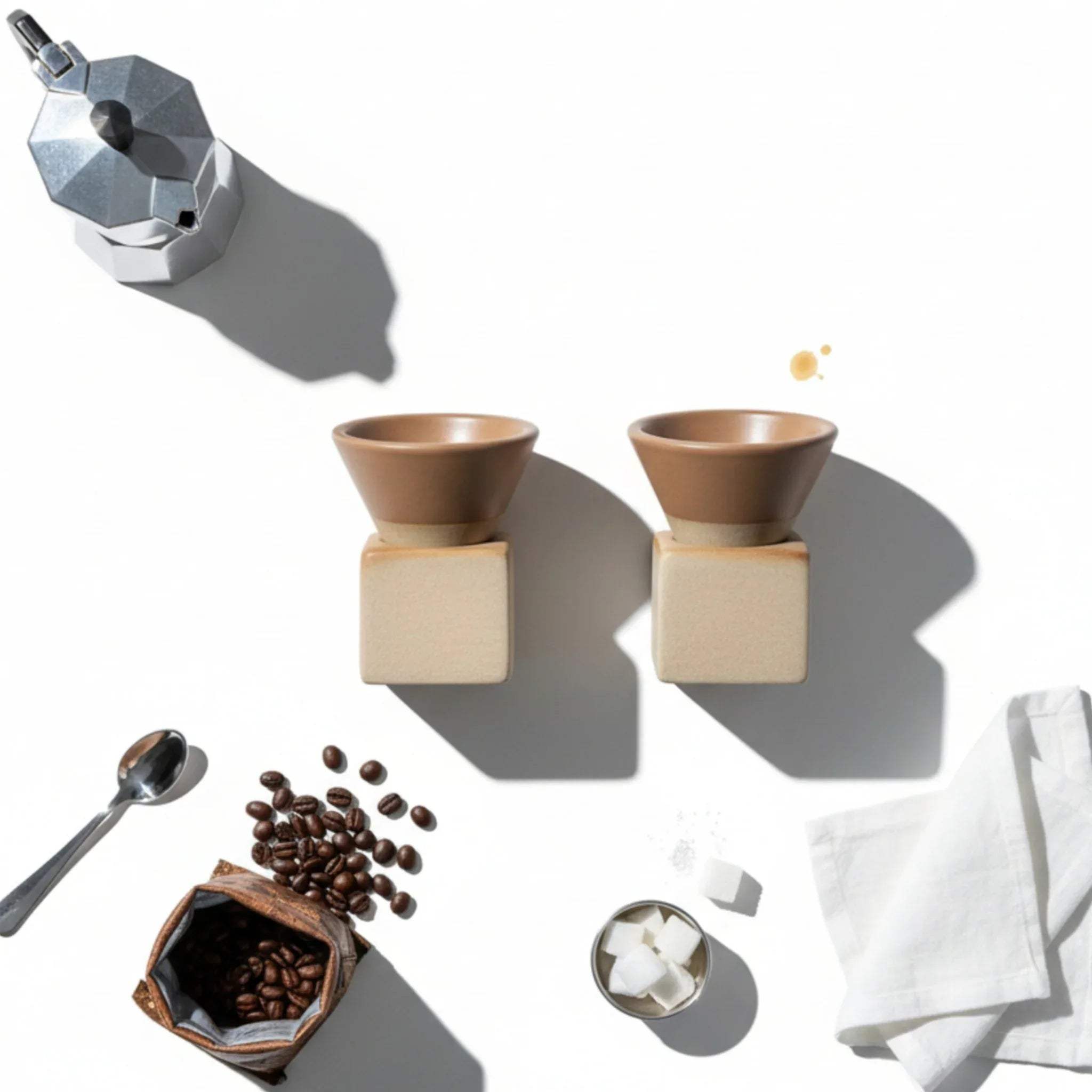 Coffee-making setup with Moka pot, coffee beans, and conical coffee cups on a white surface.