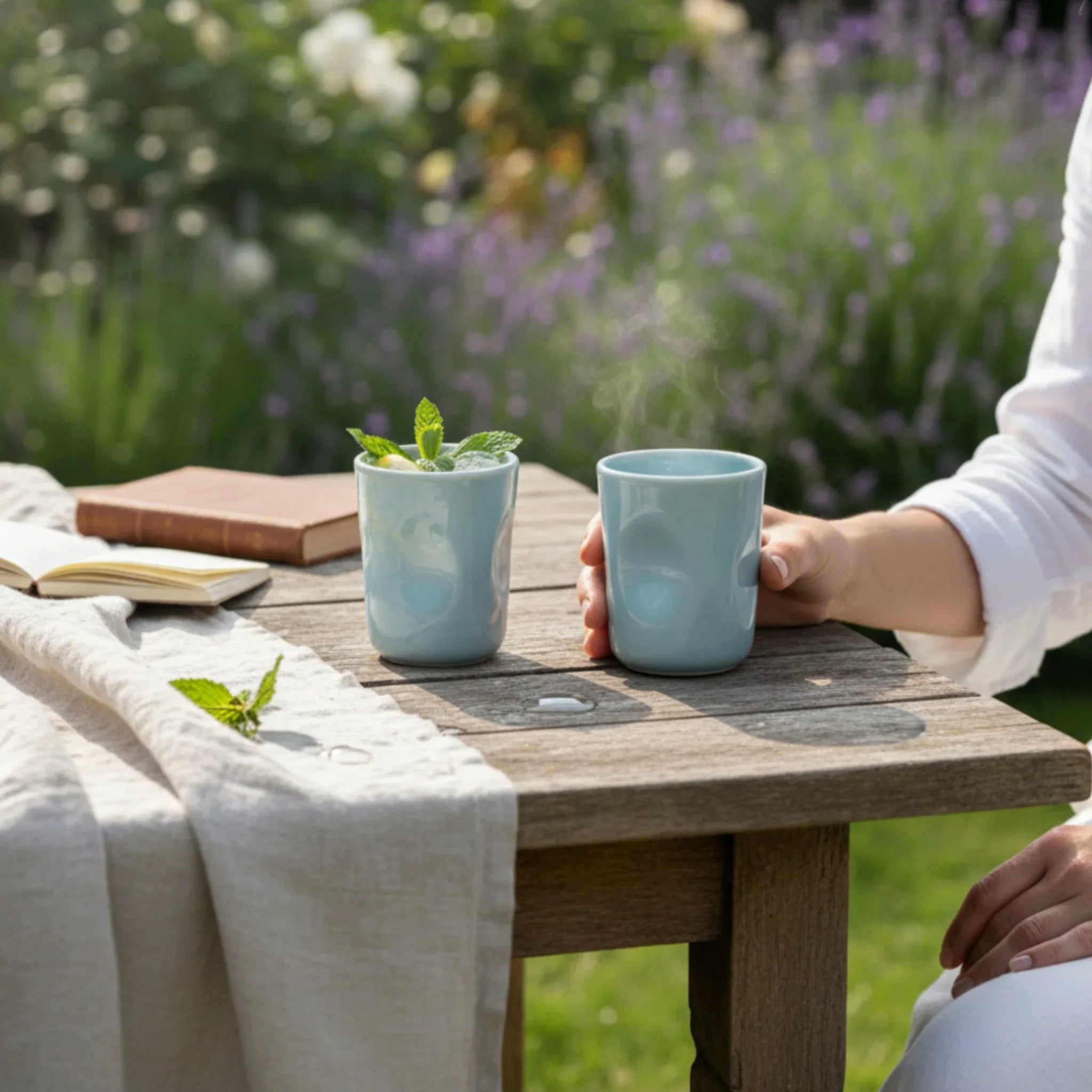 Refreshing hydration; a hand holding the sky blue glass filled with iced water and a lemon slice in a lavender garden.