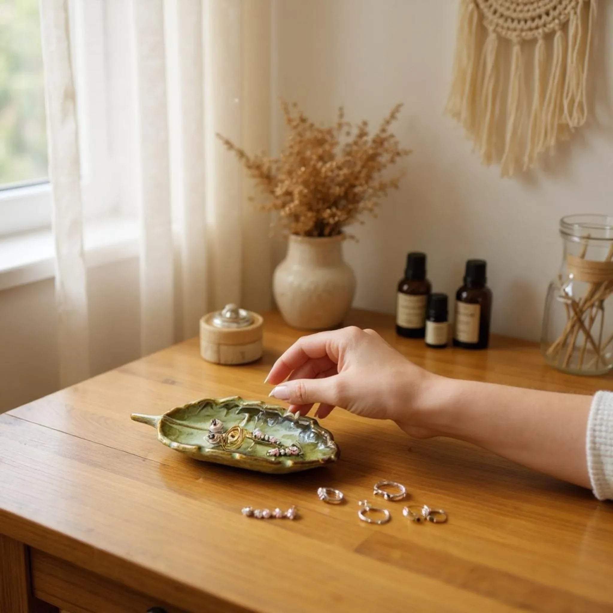 Hand arranging jewelry on a green leaf-shaped dish on a wooden table with decorative items in the background.