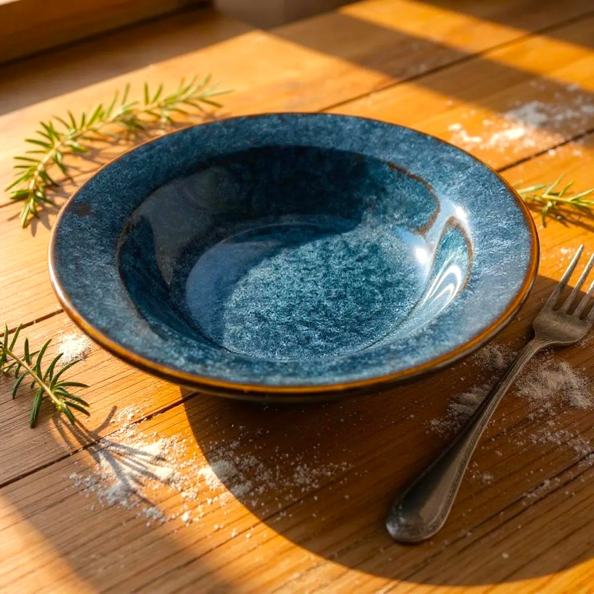 Blue ceramic bowl on a wooden surface with a fork and rosemary sprigs.