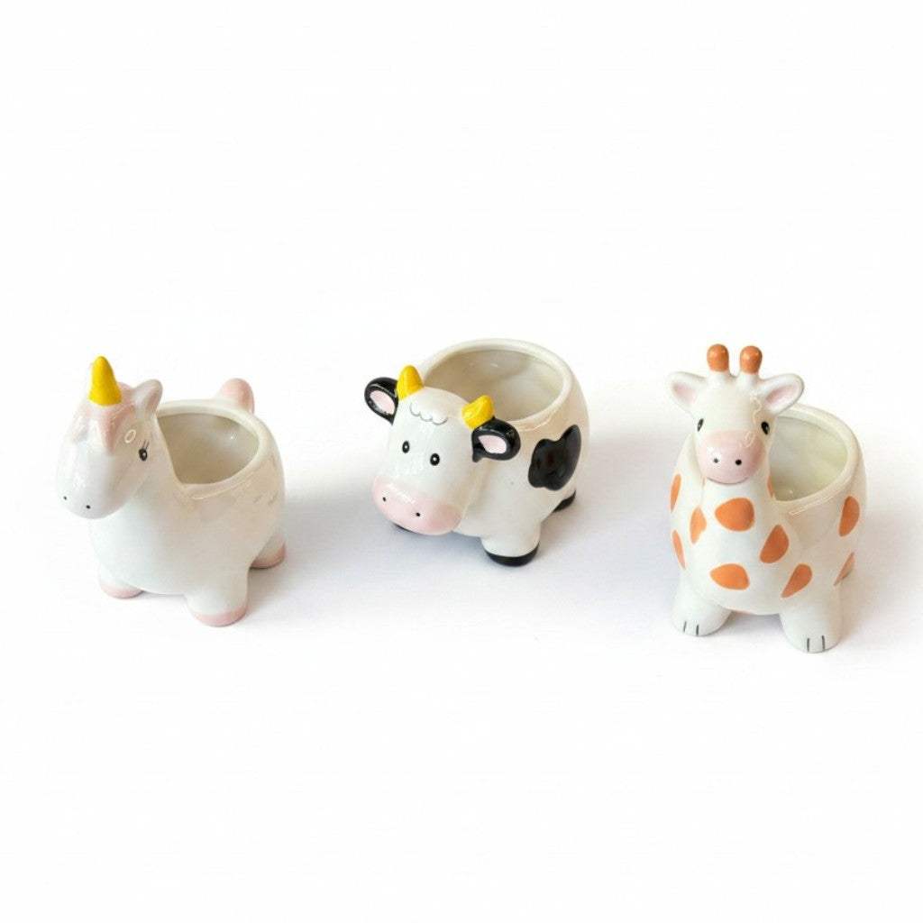 Three small white porcelain animal planters shaped like a unicorn, giraffe, and bull on a white backdrop.