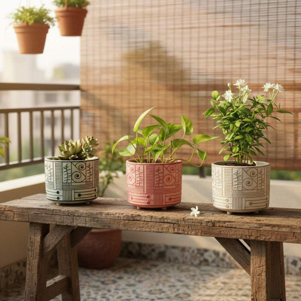 A set of three small handcrafted ceramic planters with geometric tribal carvings in green, terracotta, and cream holding indoor plants on a rustic wooden bench.