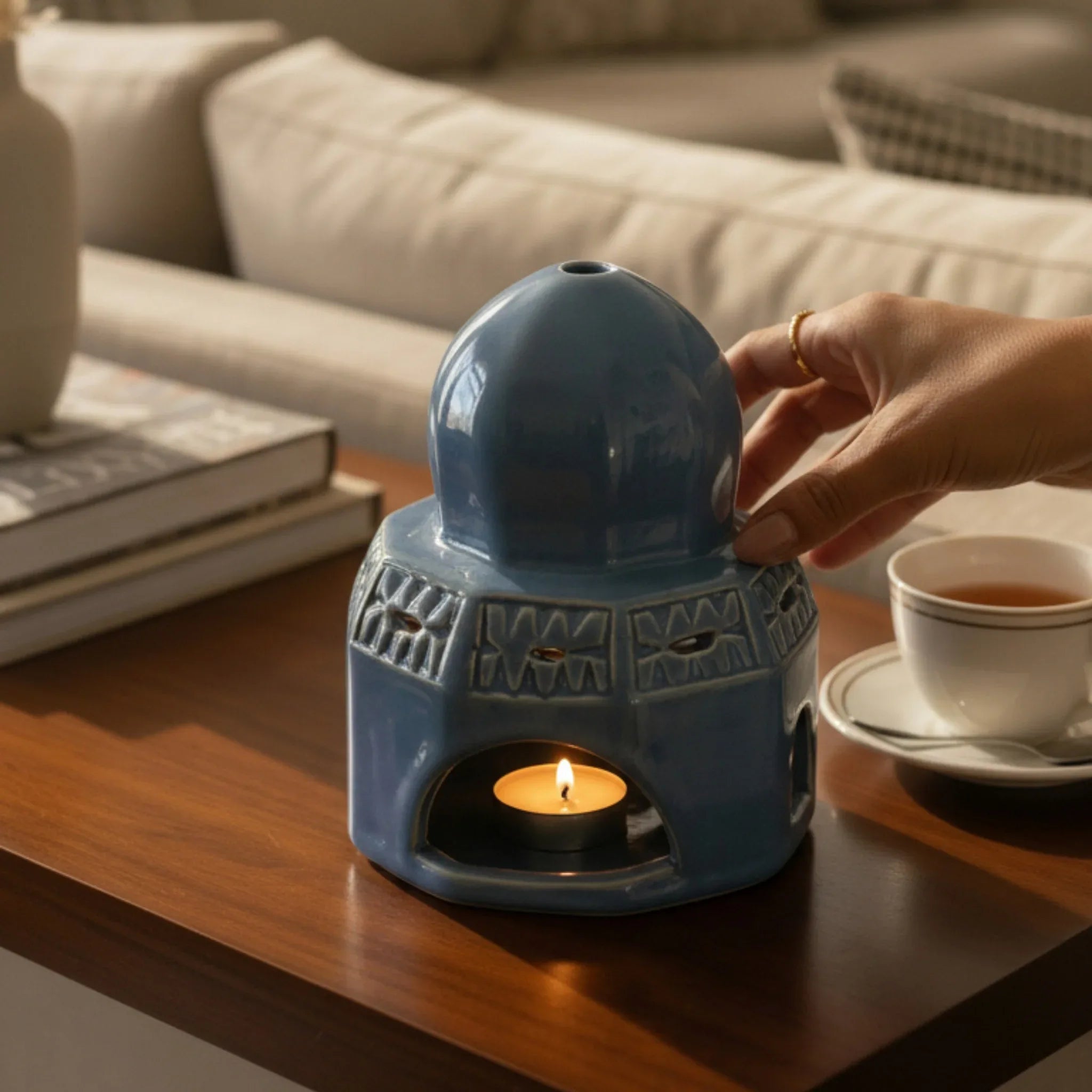 Rustic Stone blue ceramic candle holder with a lit candle on a wooden table, with a hand adjusting it.