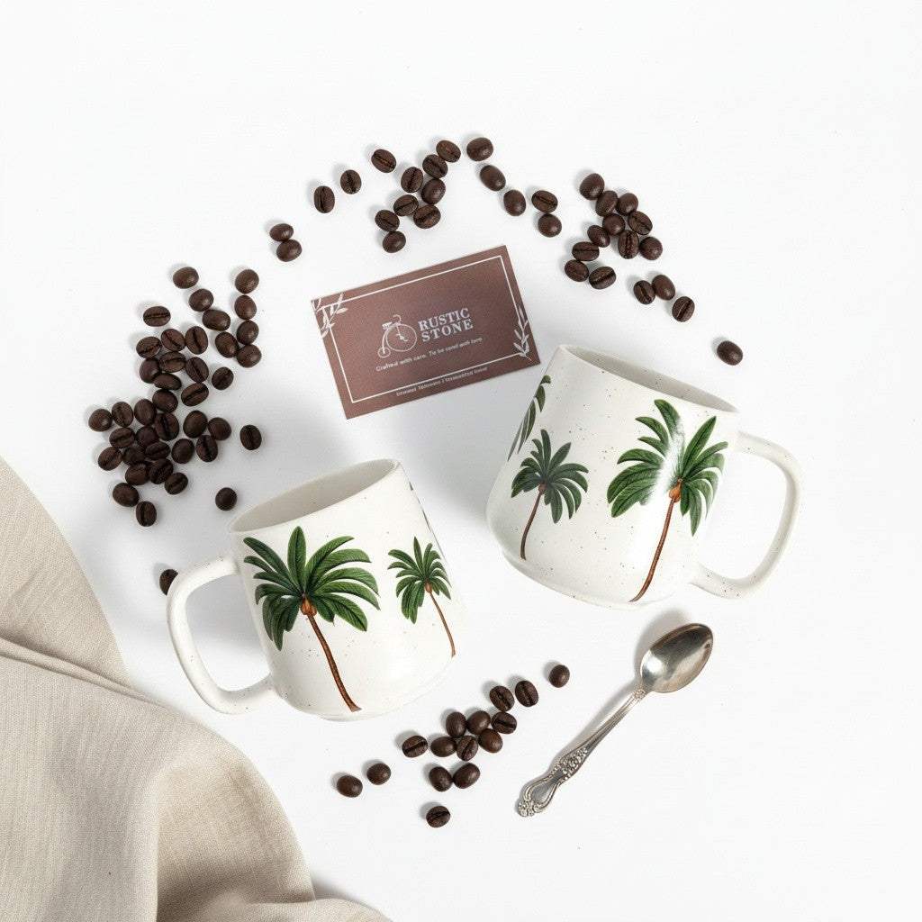 Close-up of two hand-painted palm tree ceramic mugs with a matte white speckled glaze, showcasing artisanal Indian craftsmanship.