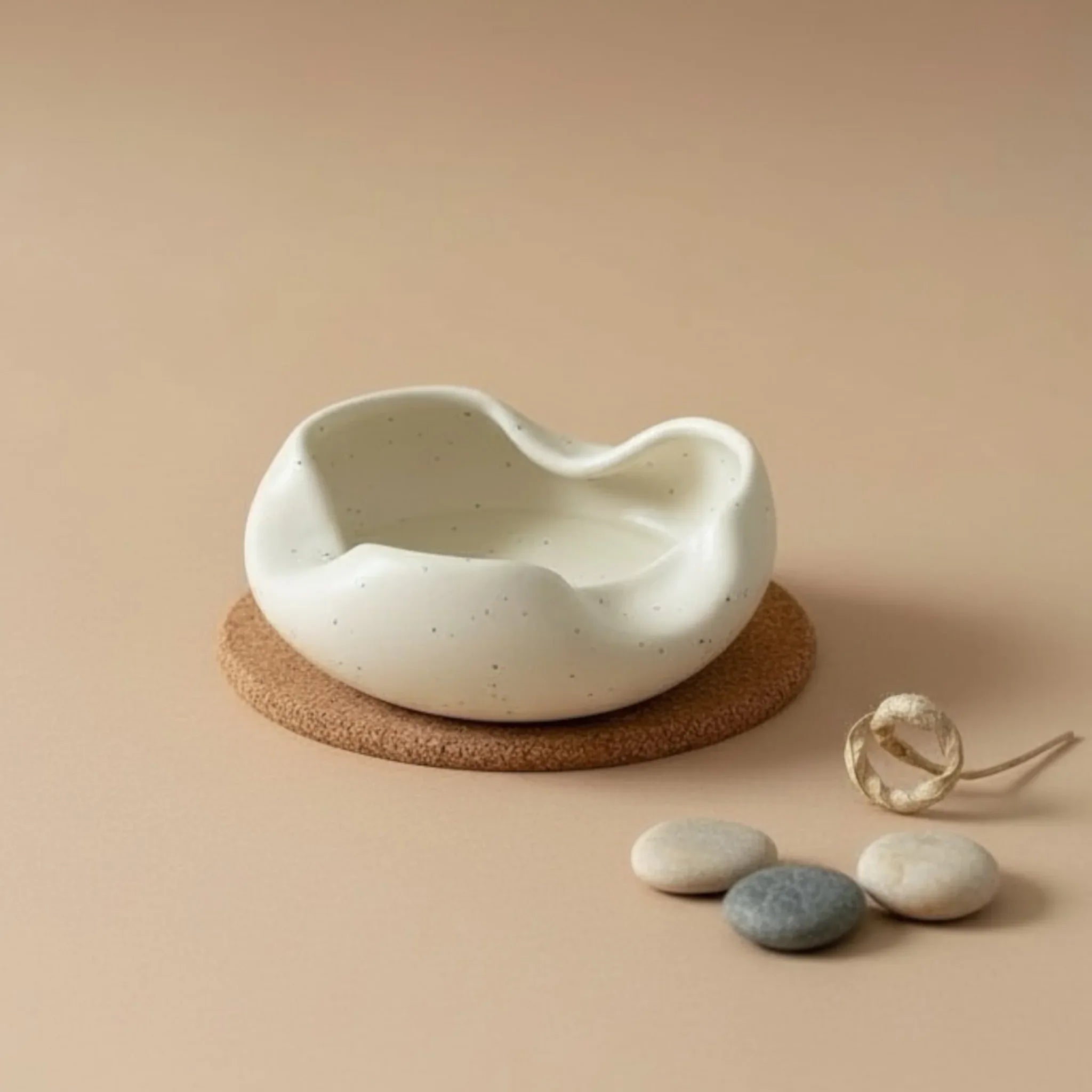White ash tray on a cork base with stones and a ring on a beige background