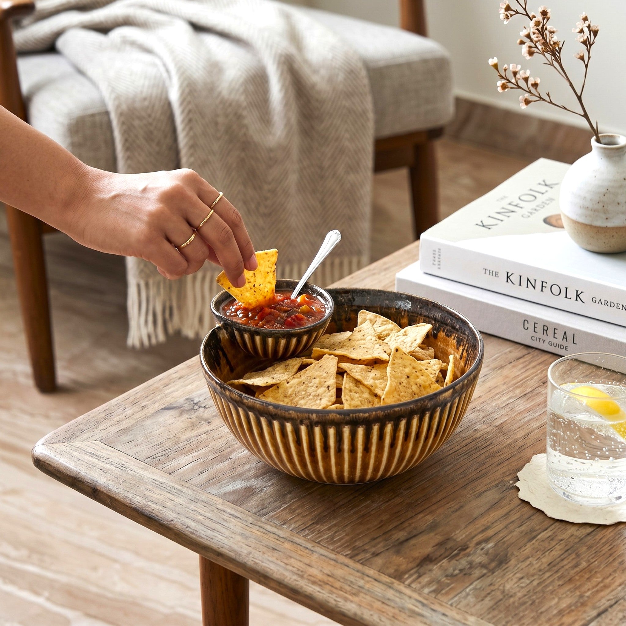 Person dipping tortilla chip into salsa with a bowl of chips inside a ceramic chip and dip bowl.